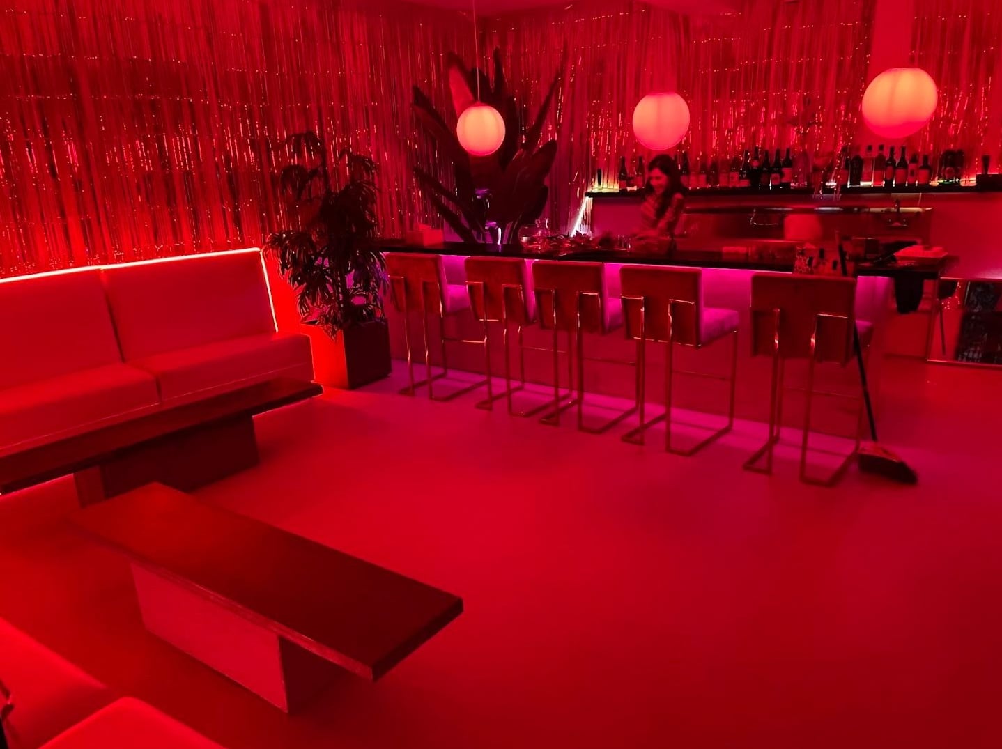 Red-lit interior of Strange Magic with bar counter, barstools, and metallic fringe decor