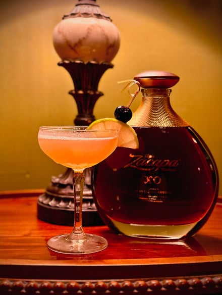 Classic daiquiri-style cocktail alongside a Zacapa XO rum bottle, with the bar's vintage lamp creating warm ambiance
