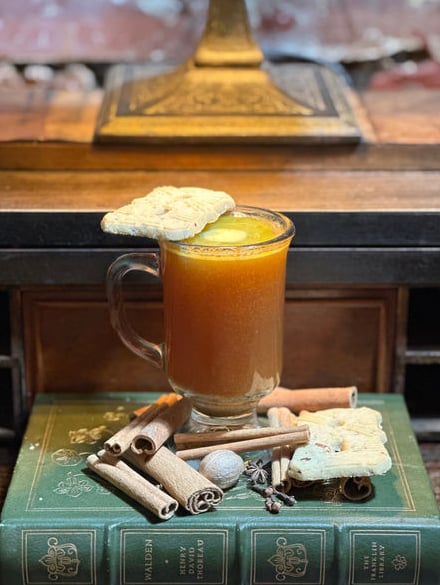 Seasonal hot cocktail garnished with spiced cookies, presented on vintage Thoreau books with cinnamon sticks