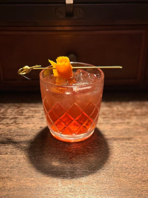 Amber spirit-based cocktail topped with an elegant curl of orange peel twist.