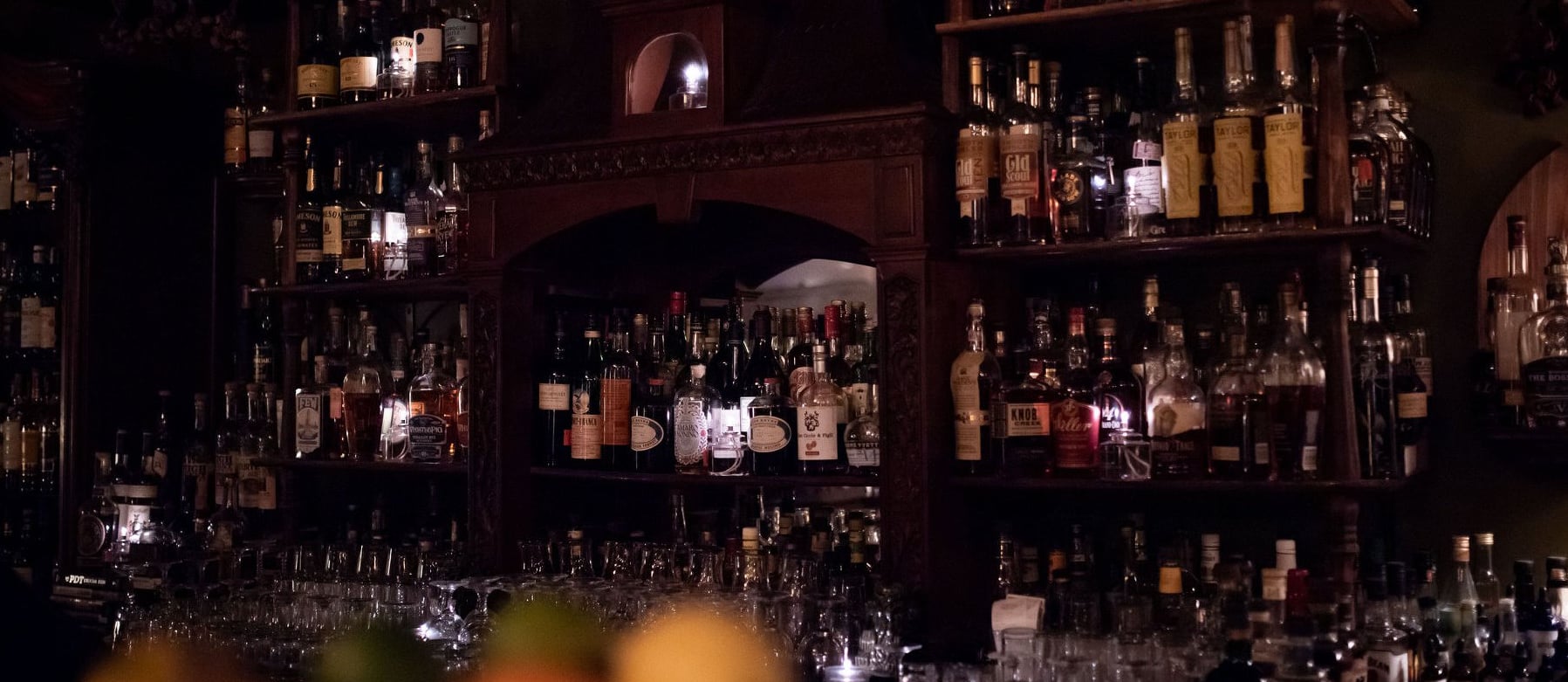Dimly lit backbar featuring an extensive selection of spirits and classic dark wood shelving.