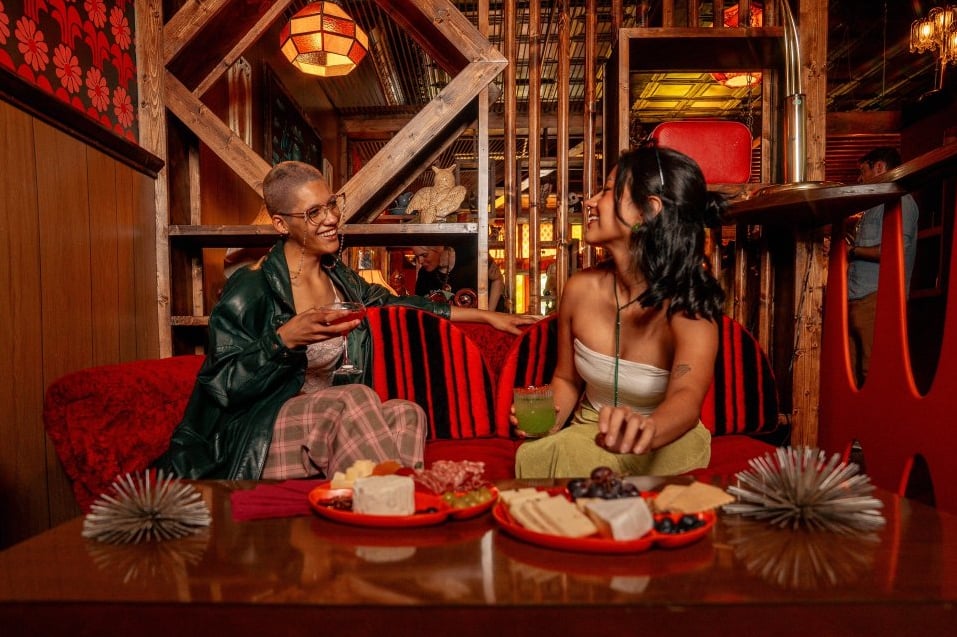 Guests sharing charcuterie and cocktails in DayTrip's red vintage lounge nook
