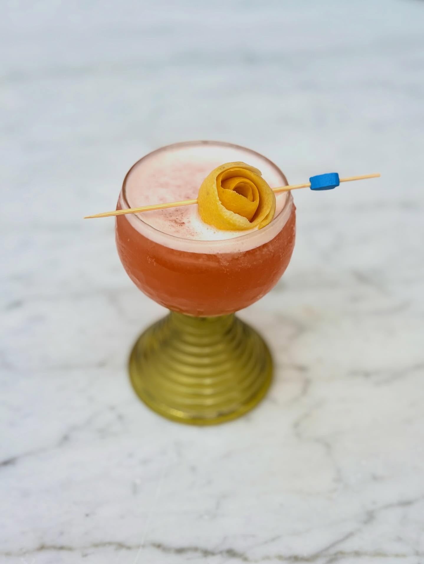 Rose-hued cocktail featuring an elegant lemon rose garnish.