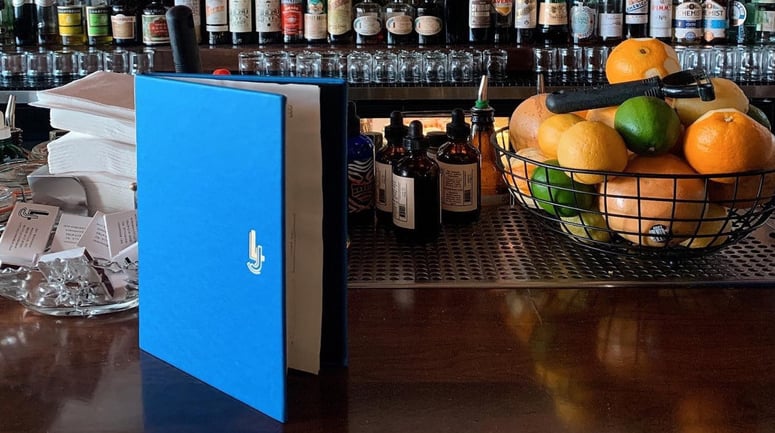 Backbar bottles, fresh citrus, and the house menu at the bar counter