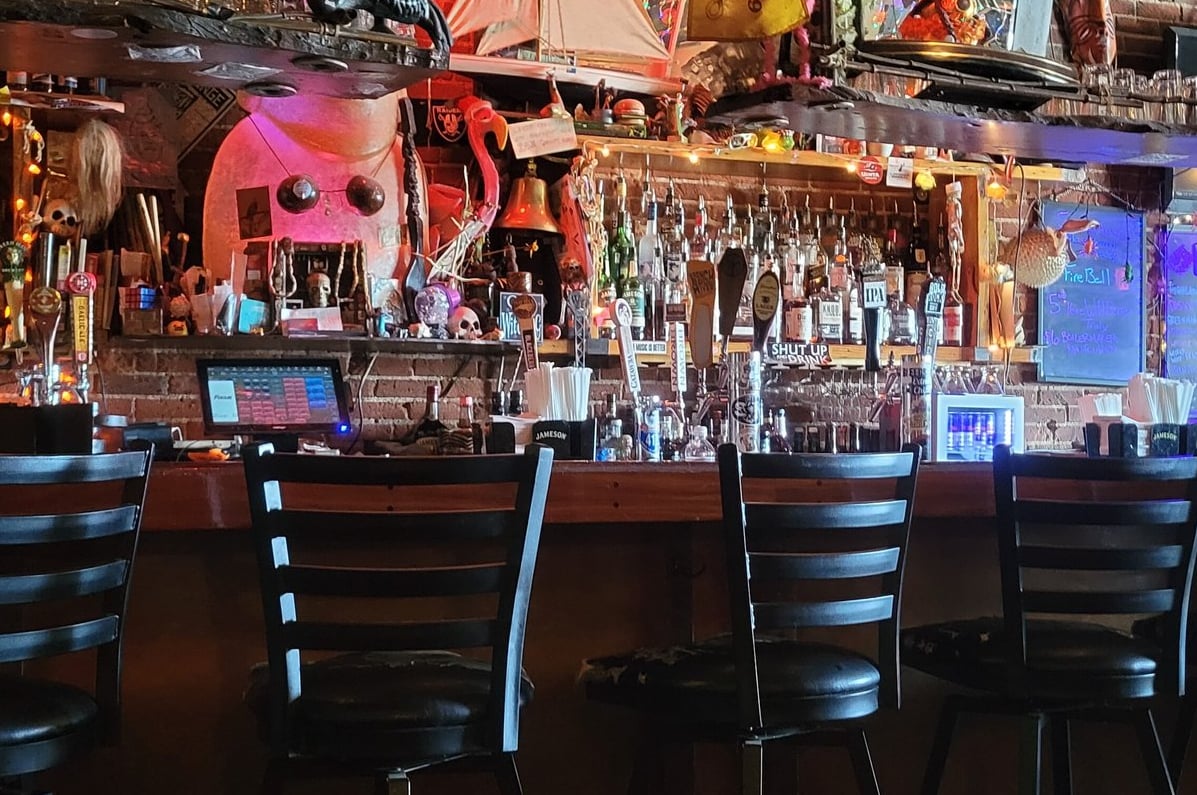 Bar counter with stools and eclectic backbar adorned with nautical collectibles under colorful mood lighting