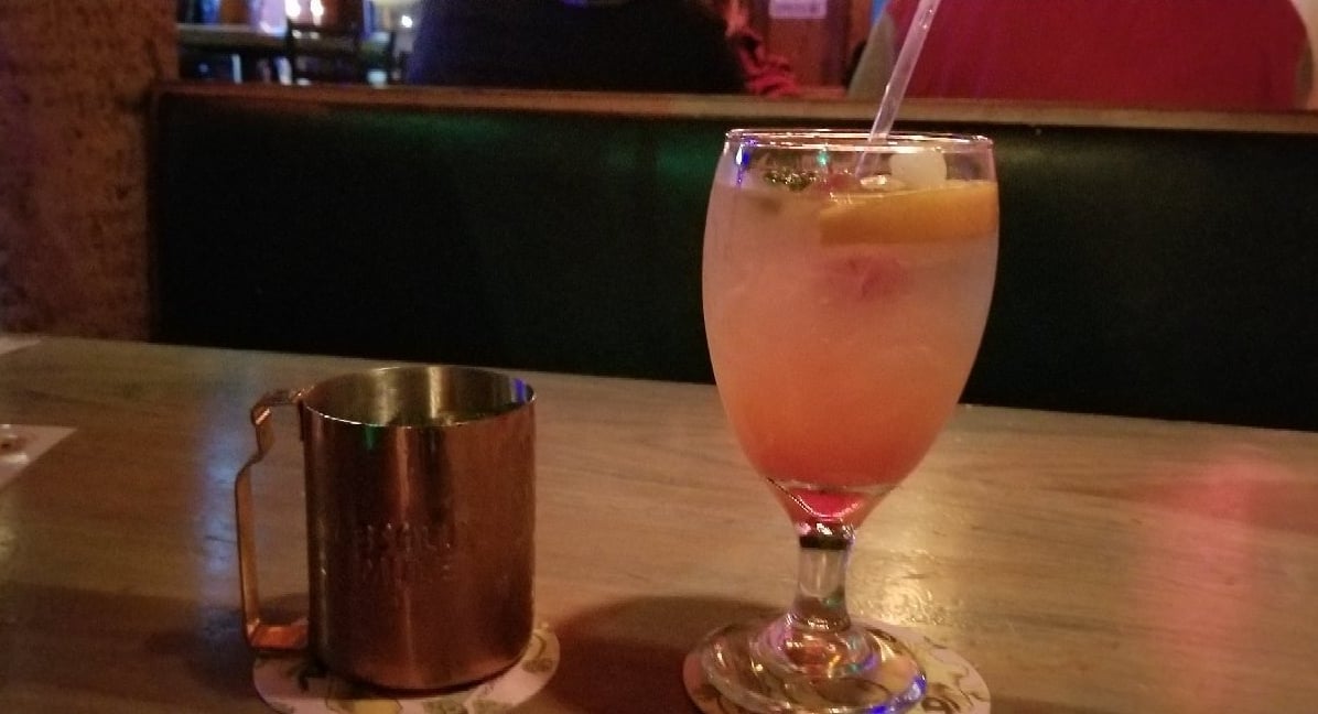 Tropical cocktail at a table with the bar's brick walls and warm lighting visible in the background