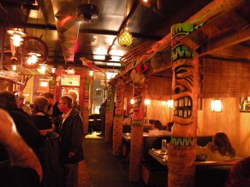 Tiki-themed interior with carved tiki poles separating the booths, corrugated metal ceiling, and warm dim lighting