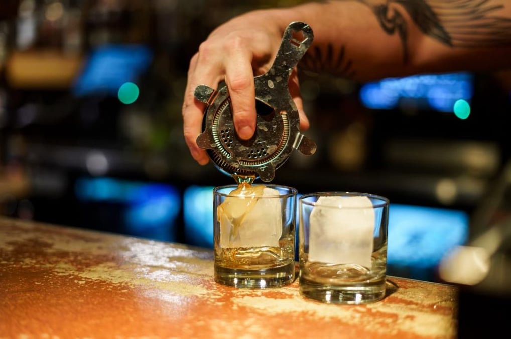 Bartender pouring fresh cocktails over large cubes.