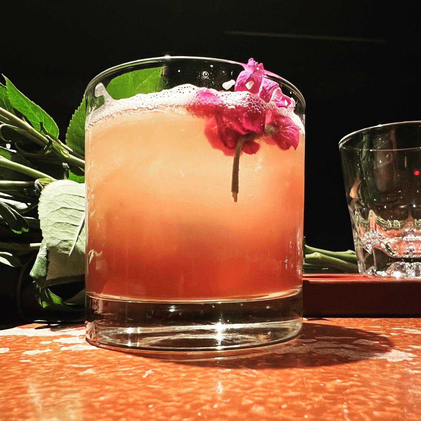 Pink signature cocktail topped with a fresh flower garnish.