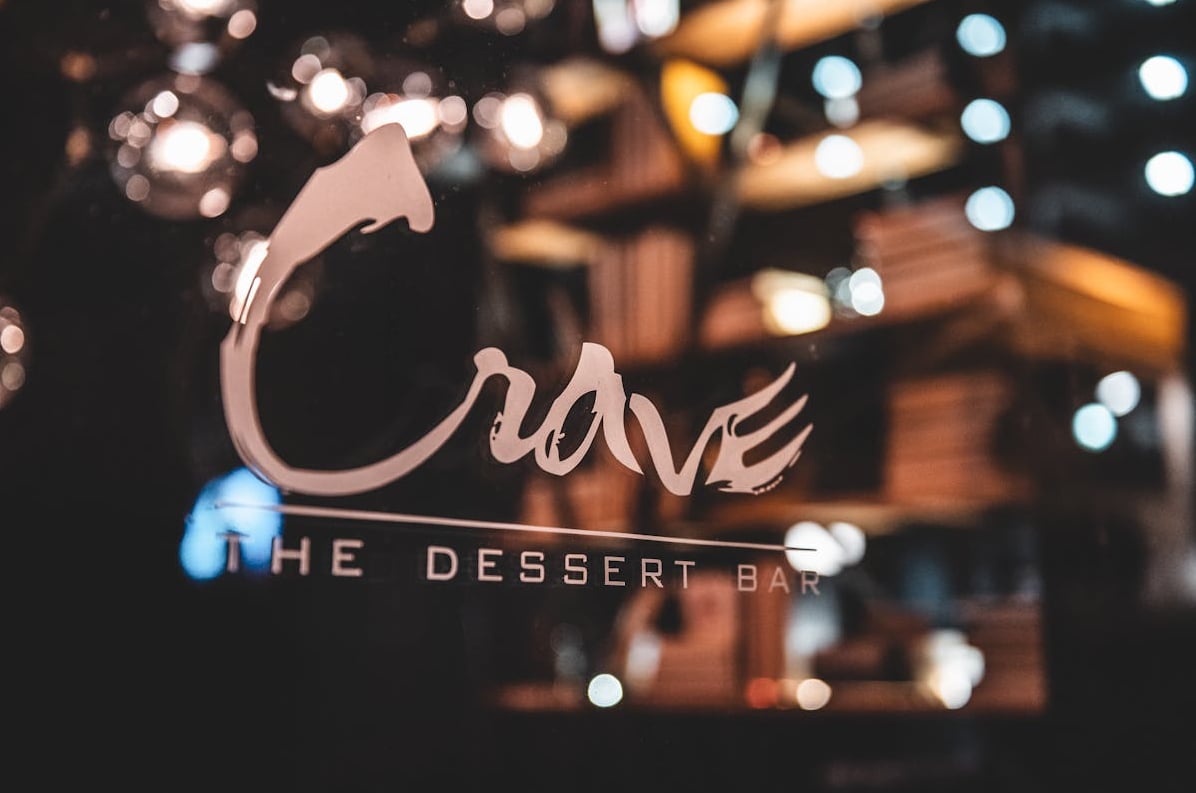 Close-up of Crave The Dessert Bar signage viewed through the entrance with warm ambient lighting.