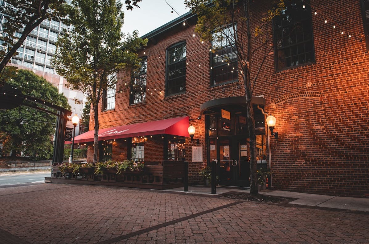 Charming brick exterior featuring a classic red awning and inviting string lights.