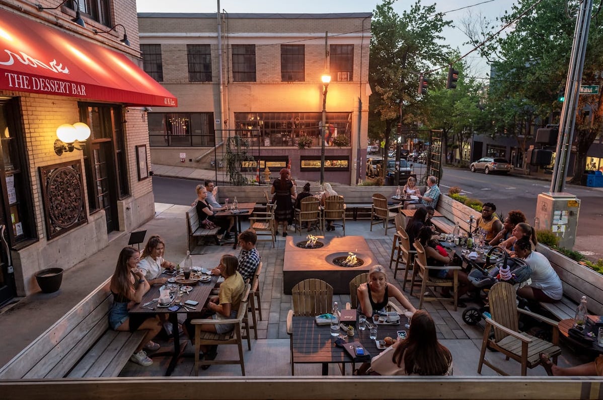 Lively outdoor patio dining at sunset featuring communal seating and fire pits.