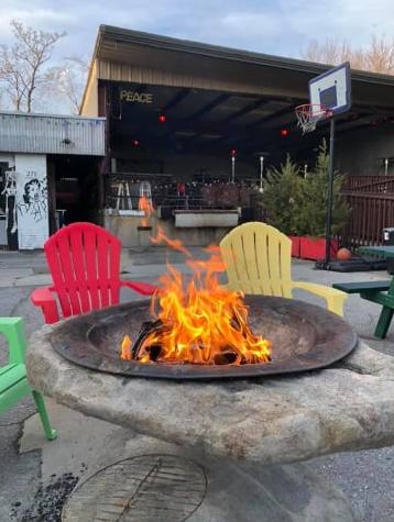 Outdoor patio fire pit surrounded by colorful Adirondack chairs, with the venue's mural-covered stage building behind