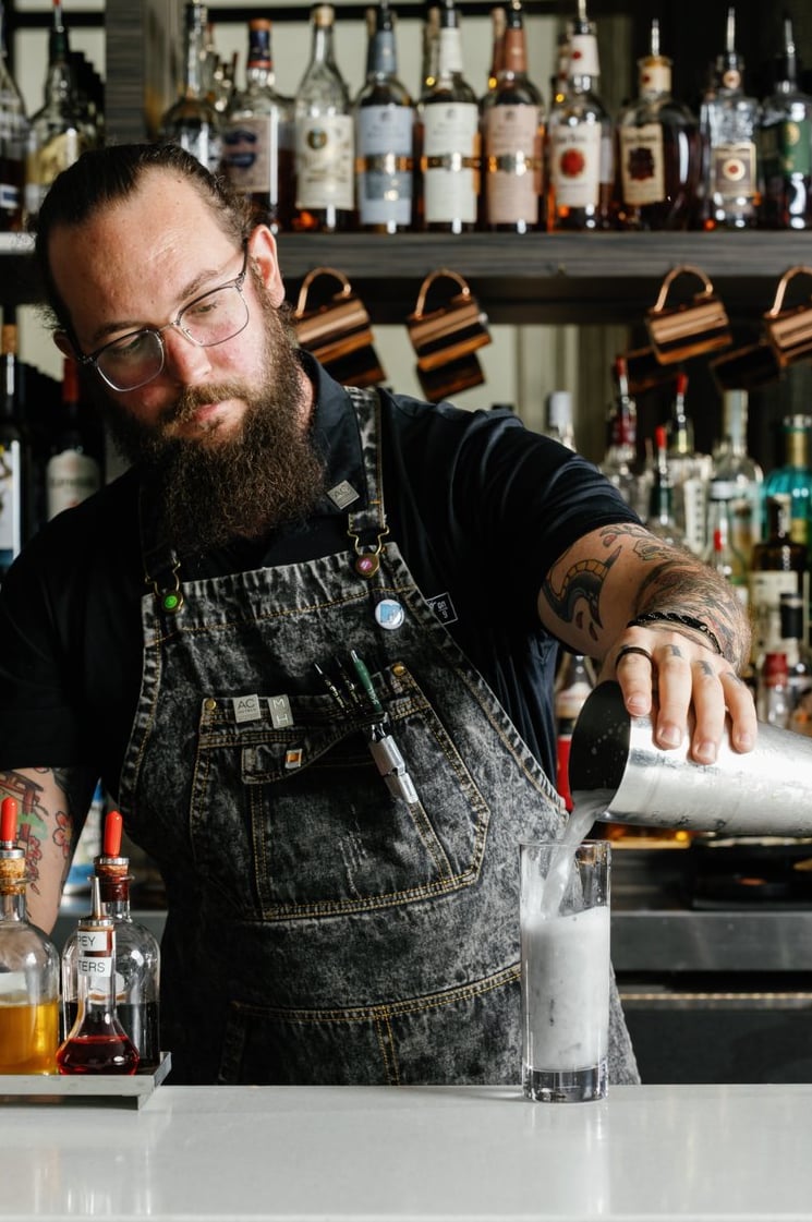 Bartender crafting a cocktail with the full spirits collection behind