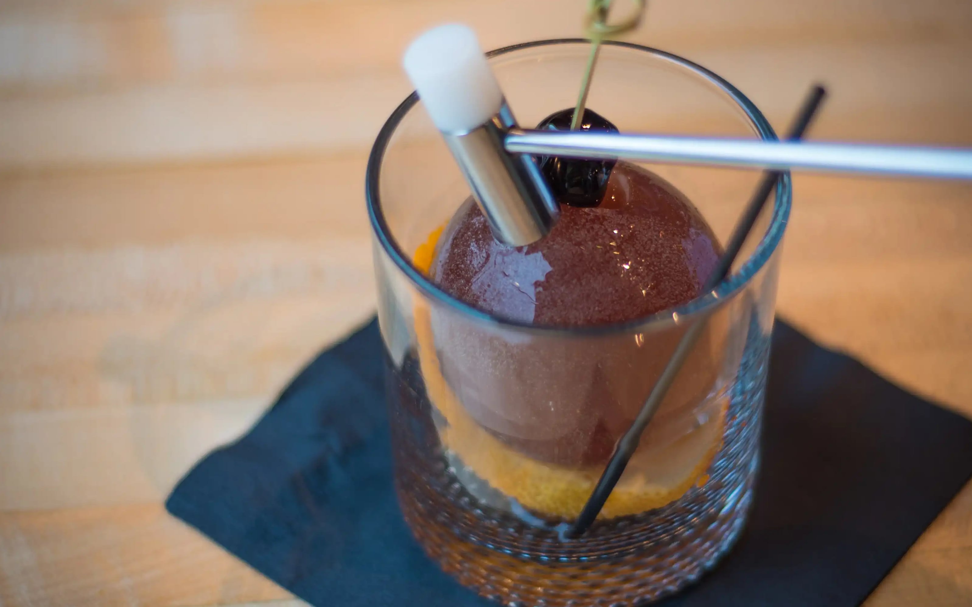 The Ice Breaker cocktail, served over a hand-carved ice sphere with cherry garnish