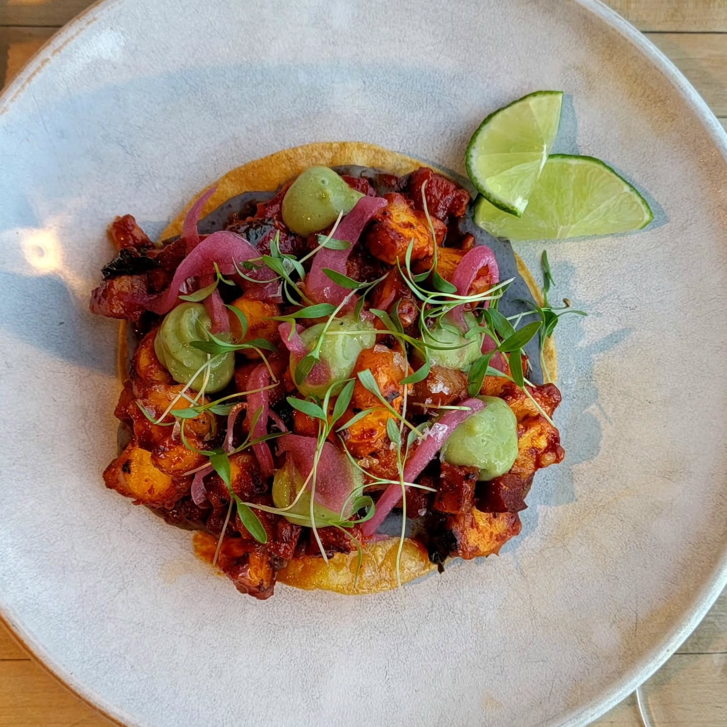 Crispy tostada topped with pickled onion, avocado crema, and lime