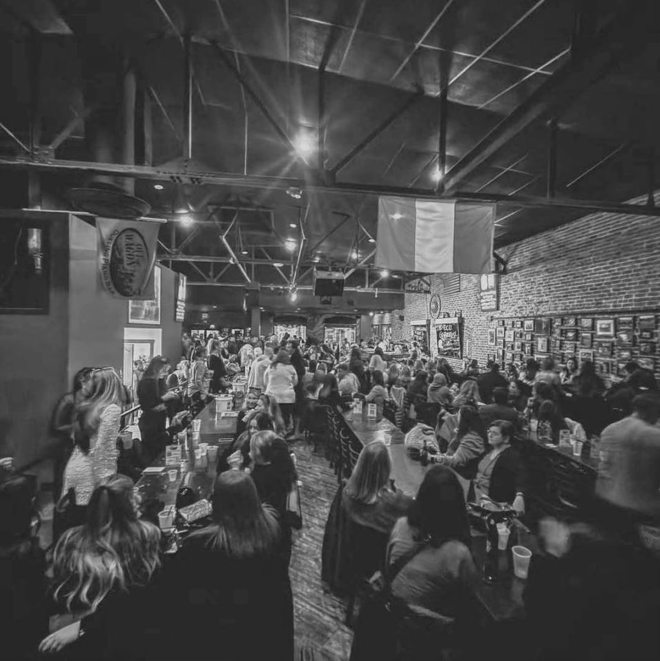Packed house at the bar with exposed brick walls and dueling piano stage lights